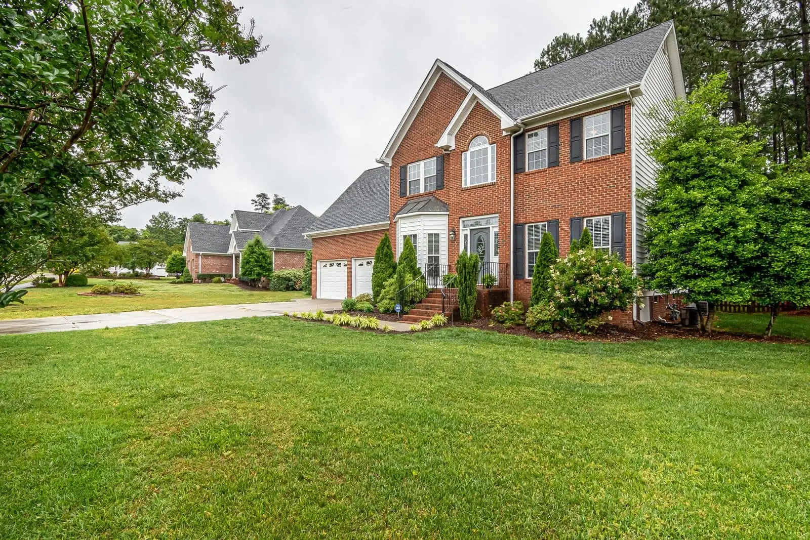 A two-story brick house with black shutters, a wide front lawn and a paved drive, the kind of home a real estate auction lot page describes.
