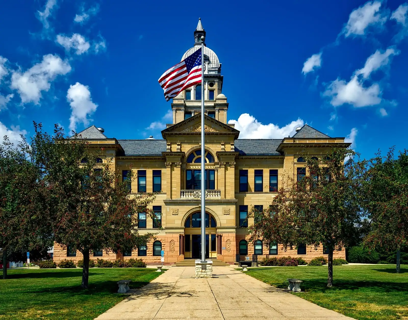 A historic county courthouse with an American flag against a blue sky, the kind of building where many foreclosure and court-ordered sales are held.