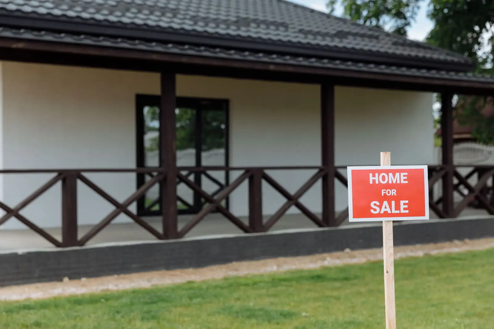A white house with a porch and a red home for sale sign on the lawn, the kind of property a lot page carries.