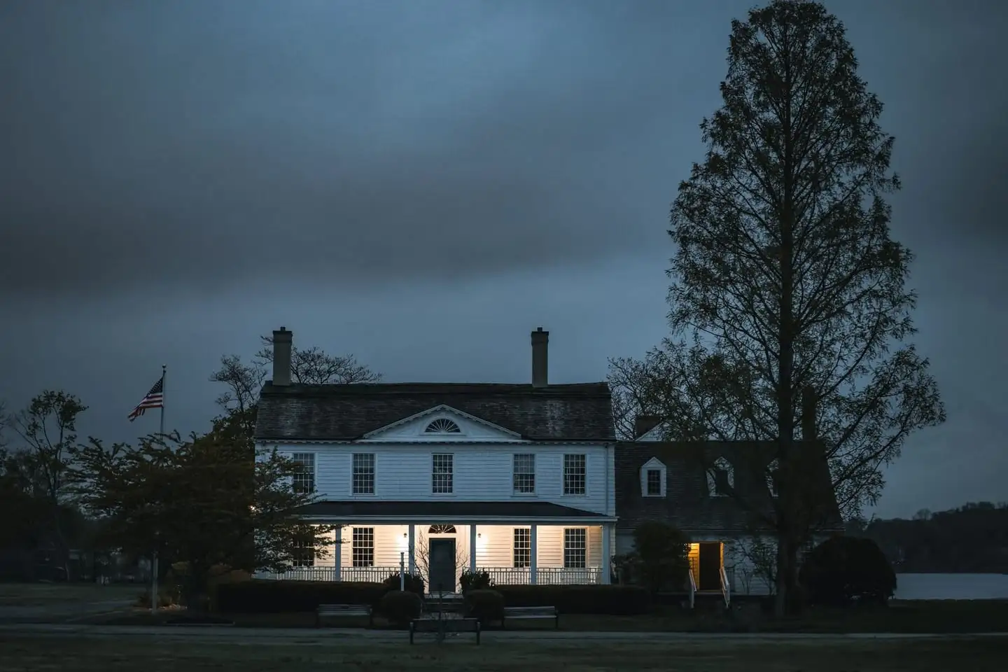 A colonial house at dusk with lights on, the kind of property sold at a foreclosure or REO auction.